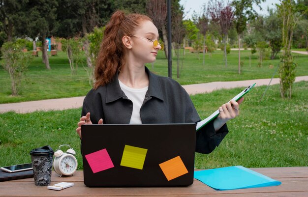 Chica con el pelo rojo trabajando en la computadora portátil con carpeta