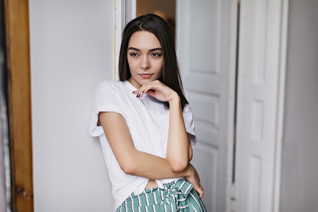 Chica pensativa con hermoso cabello oscuro mirando a otro lado. Foto interior de mujer caucásica inspirada relajándose en casa en fin de semana.