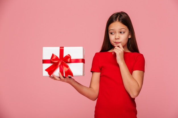 Chica pensativa mirando el regalo en mano y pensando en ello aislado