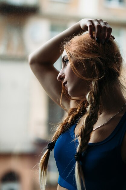 Chica pensativa en un traje de gimnasio plantea delante de una ventana en un gimnasio