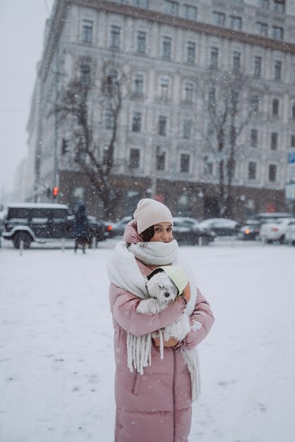 Chica con un perro en sus brazos en una calle de la ciudad, la nieve está cayendo