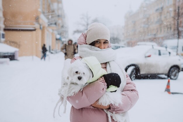 Chica con un perro en sus brazos mientras cae nieve