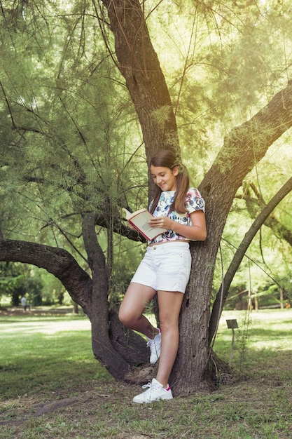 Foto gratuita chica de pie cerca de la lectura del árbol