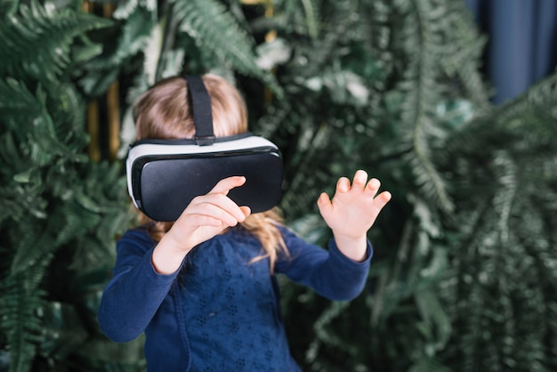 Chica de pie cerca de las plantas con gafas de realidad virtual tocando las manos en el aire