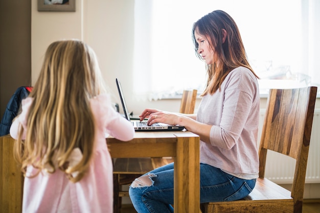 Foto gratuita chica de pie delante de su madre trabajando en la computadora portátil