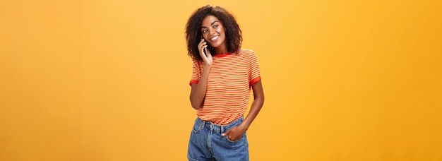 Chica de piel oscura con estilo haciendo una llamada telefónica informal a un amigo contándole todos los detalles de después de un da romántico
