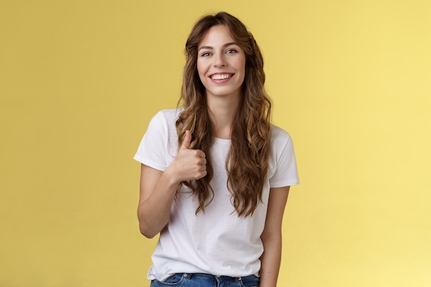 La chica piensa que hiciste un gran trabajo. Sonriente, alegre, guapa, mujer, largo, rizado, corte de pelo, aprobar, elección perfecta, dar, pulgar, arriba, de acuerdo, como, su, estilo, sonriente, apoyo, excelente, idea, fondo amarillo