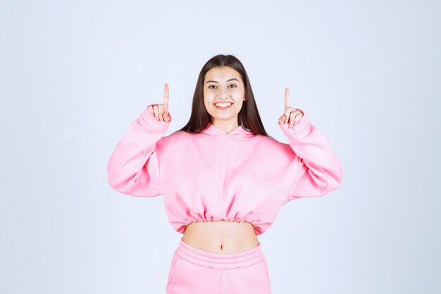 Chica en pijama rosa apuntando al piso de arriba con cara emocional