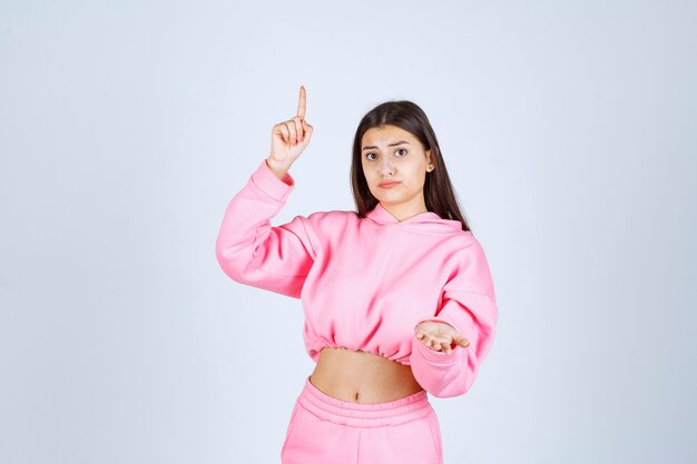 Chica en pijama rosa apuntando hacia arriba