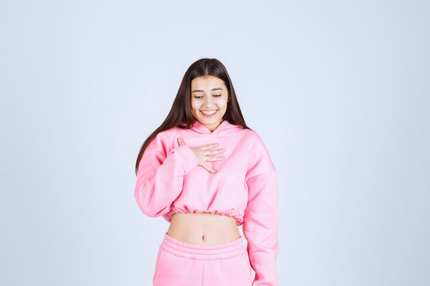 Chica en pijama rosa apuntando a sí misma y parece sorprendida.