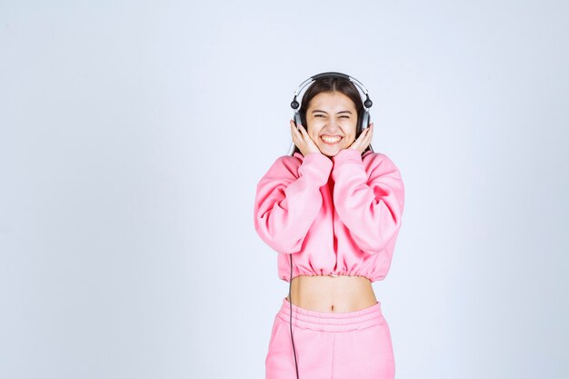 Chica en pijama rosa escuchando los auriculares y divirtiéndose. Foto de alta calidad