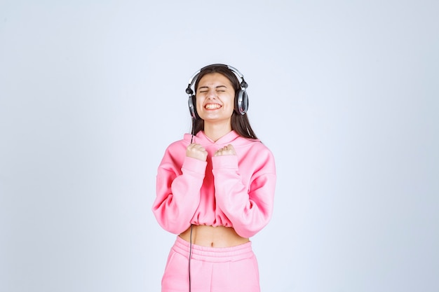 Chica en pijama rosa escuchando los auriculares y divirtiéndose. Foto de alta calidad