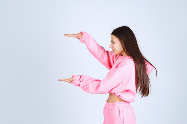 Chica en pijama rosa mostrando la cantidad estimada o el tamaño de un producto