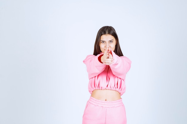 Foto gratuita chica en pijama rosa mostrando signo de pistola en la mano