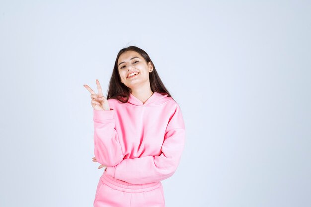 Chica en pijama rosa se siente feliz y muestra un signo de mano positivo.