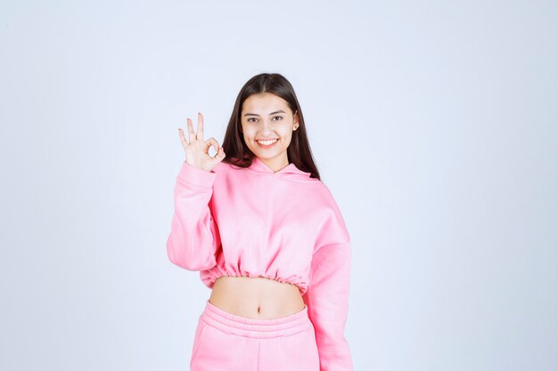 Chica en pijama rosa se siente feliz y muestra un signo de mano positivo.