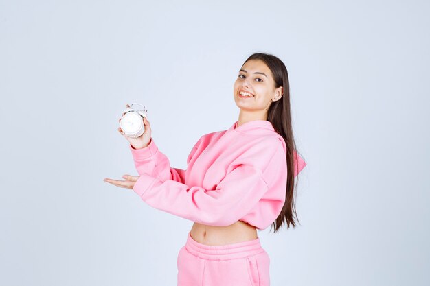 Chica en pijama rosa sosteniendo un despertador y promocionándolo como producto.