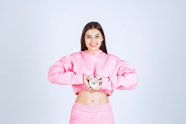 Chica en pijama rosa sosteniendo un despertador y promocionándolo como producto.