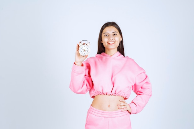 Chica en pijama rosa sosteniendo un despertador y promocionándolo como producto.