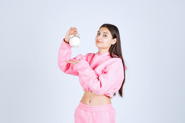 Chica en pijama rosa sosteniendo un despertador y promocionándolo como producto.