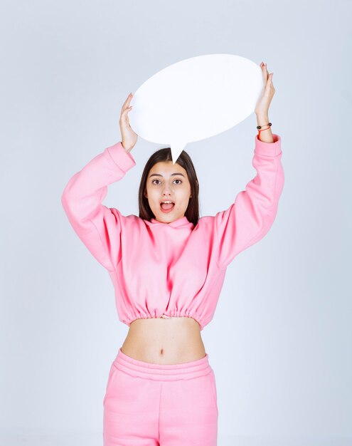 Chica en pijama rosa sosteniendo una pizarra redonda sobre su cabeza.