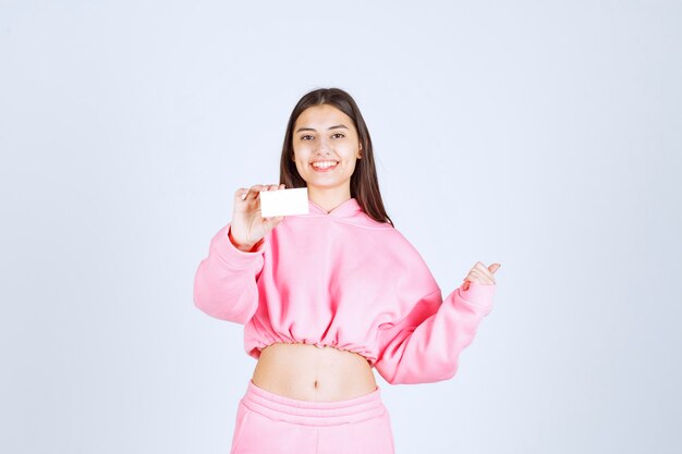 Chica en pijama rosa sosteniendo una tarjeta de visita y apuntando a otra persona.