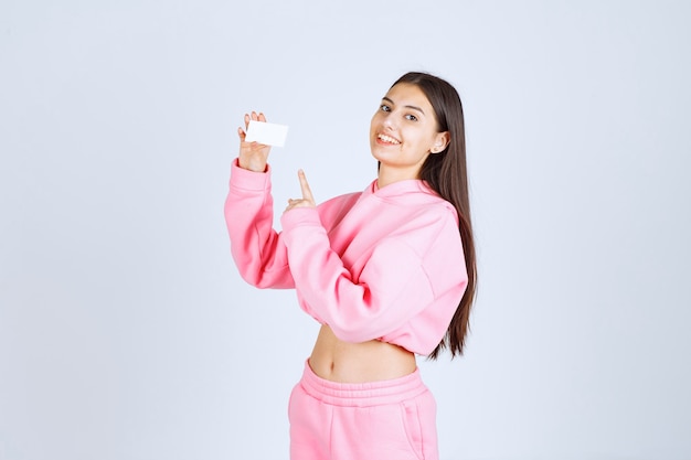 Chica en pijama rosa sosteniendo una tarjeta de visita y presentándose a sus socios comerciales.