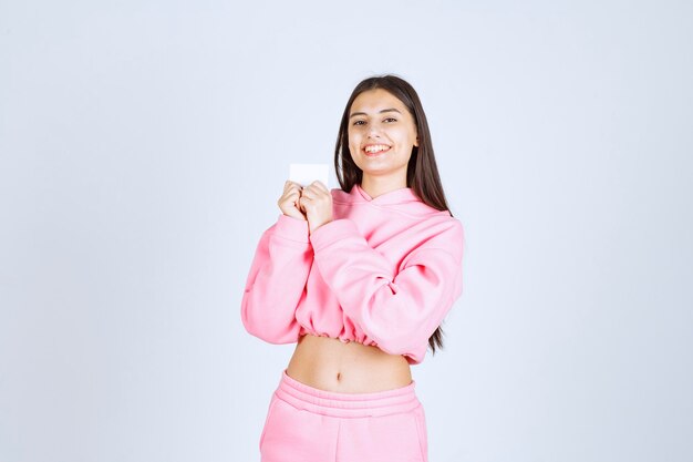 Chica en pijama rosa sosteniendo una tarjeta de visita y presentándose a sus socios comerciales.