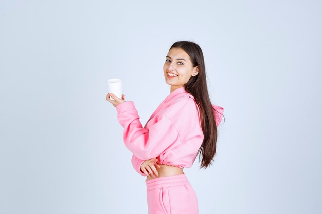 Chica en pijama rosa sosteniendo una taza de café y apuntando a algo