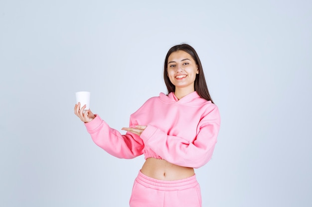 Chica en pijama rosa sosteniendo una taza de café y apuntando a algo