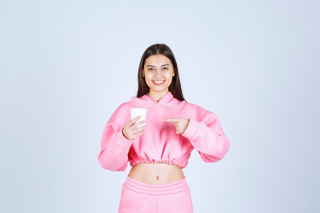 Chica en pijama rosa sosteniendo una taza de café y apuntando a algo