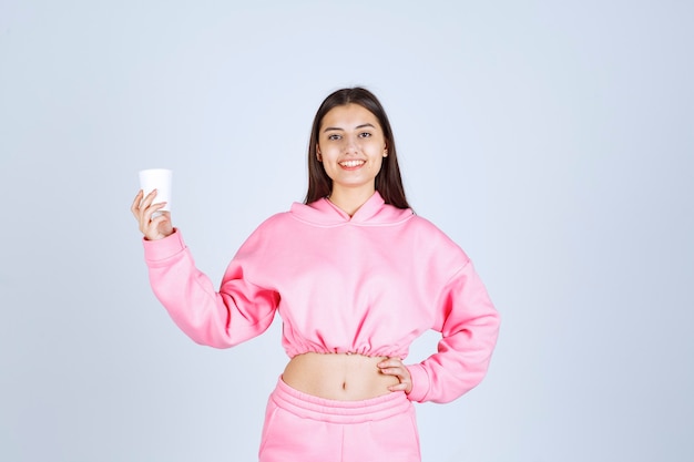 Chica en pijama rosa sosteniendo una taza de café y apuntando a algo