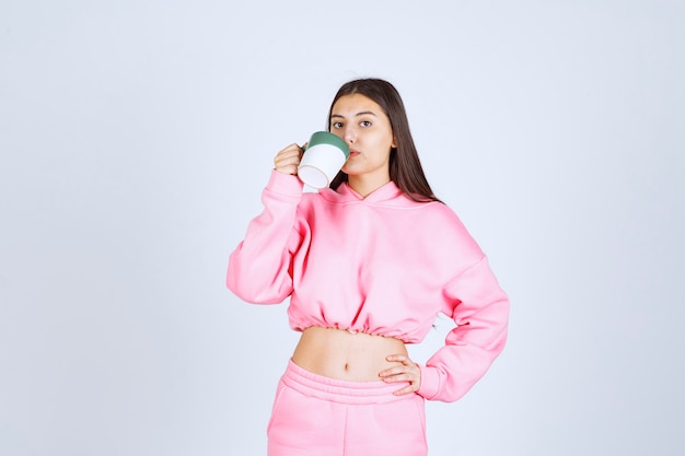 Chica en pijama rosa sosteniendo una taza de café y bebiéndola.