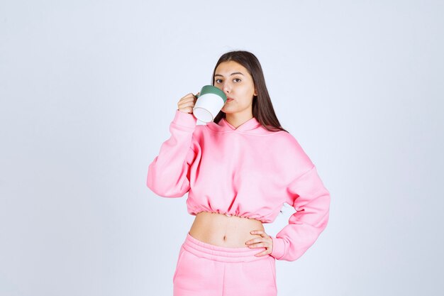 Chica en pijama rosa sosteniendo una taza de café y bebiéndola.