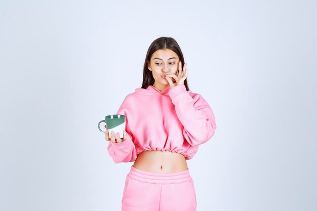 Chica en pijama rosa sosteniendo una taza de café y disfrutando del sabor.