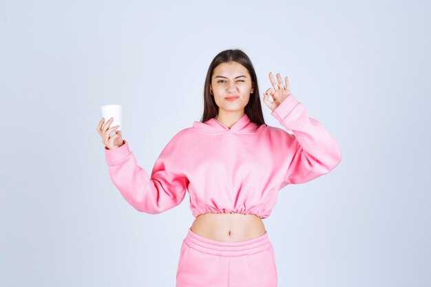 Chica en pijama rosa sosteniendo una taza de café y disfrutando del sabor