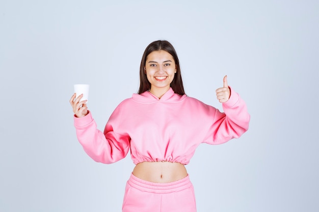 Chica en pijama rosa sosteniendo una taza de café y disfrutando del sabor