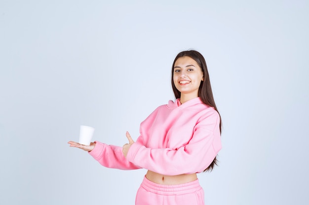 Chica en pijama rosa sosteniendo una taza de café y disfrutando del sabor