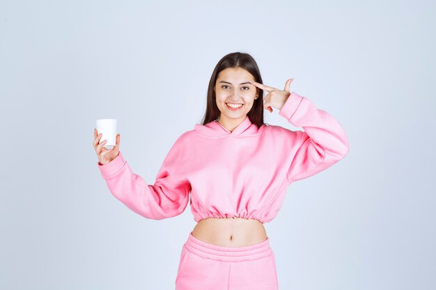 Chica en pijama rosa sosteniendo una taza de café y pensando