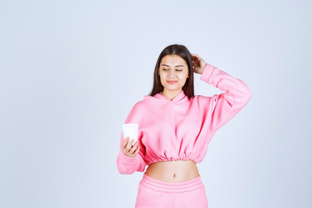 Chica en pijama rosa sosteniendo una taza de café y pensando