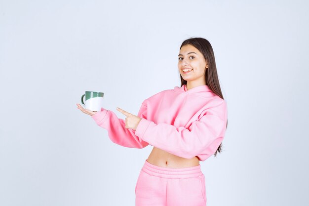 Chica en pijama rosa sosteniendo una taza de café y sintiéndose feliz.