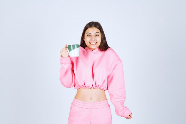 Chica en pijama rosa sosteniendo una taza de café y sintiéndose feliz.