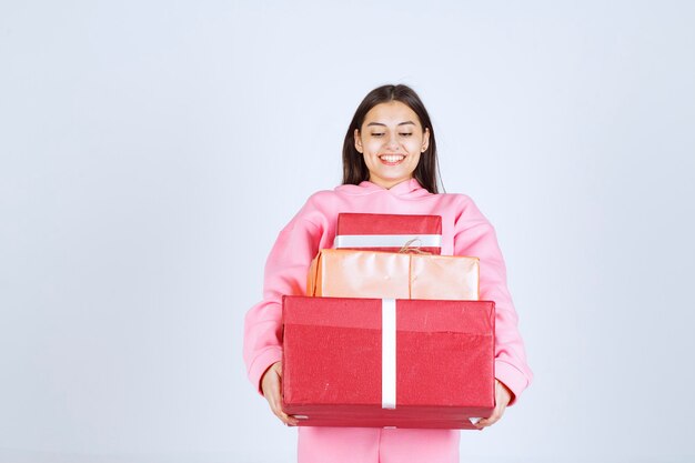 Chica en pijama rosa sosteniendo varias cajas de regalo rojas y sintiéndose feliz.