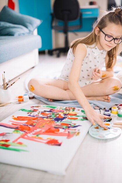 Chica pintando con los dedos sobre lienzo en piso