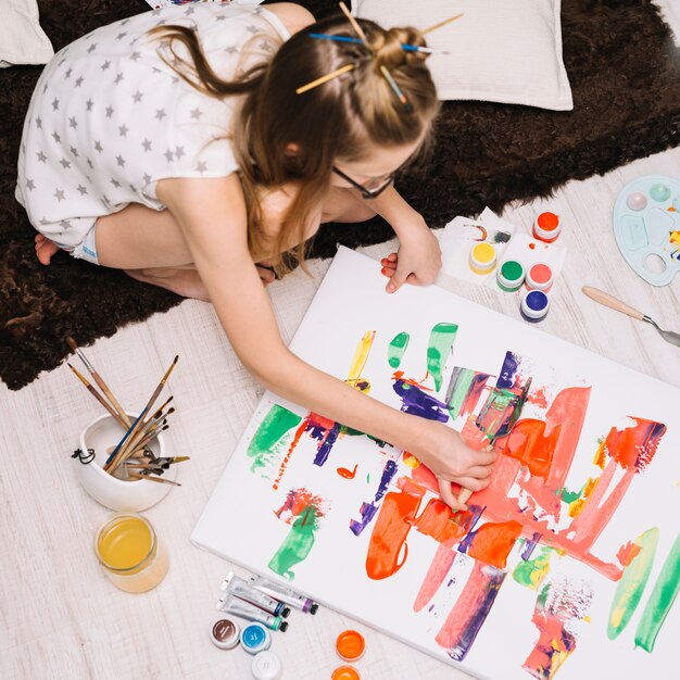 Chica pintando con gouache brillante sobre papel en piso