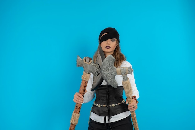 Chica pirata confiada sosteniendo hachas de guerra y mirándolas. foto de alta calidad
