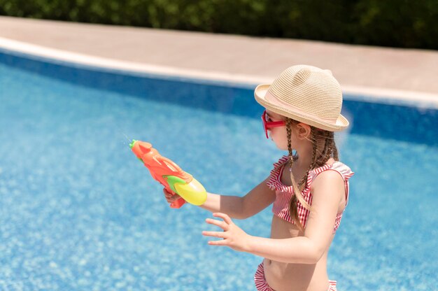 Chica en la piscina jugando con pistola de agua