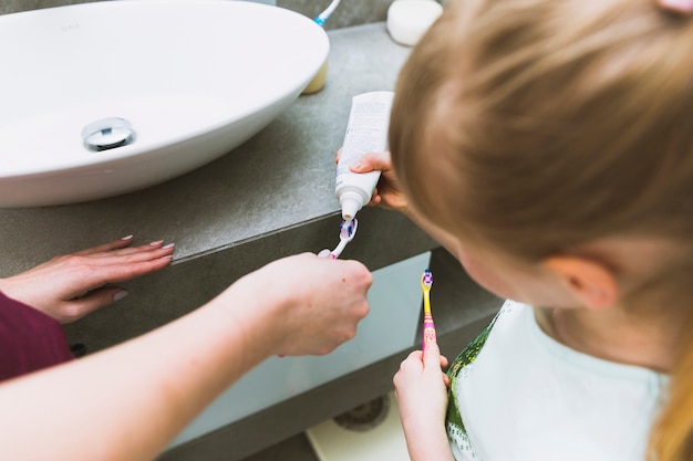 Foto gratuita chica poner pasta de dientes en el cepillo de la madre