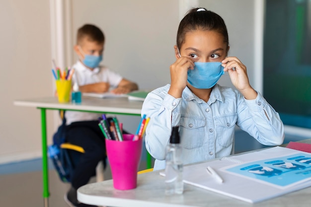 Chica poniéndose su mascarilla médica en clase