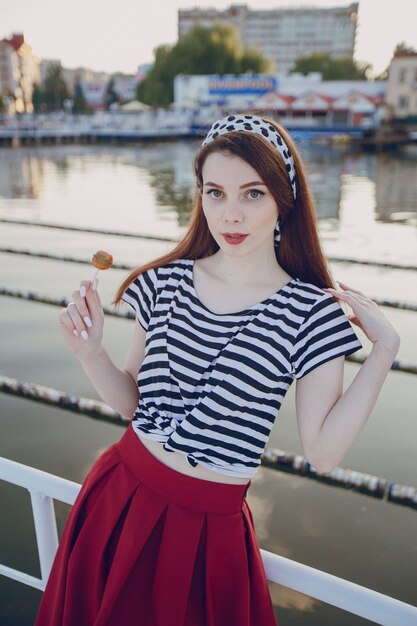 Chica posando apoyada en una valla blanca con agua de fondo